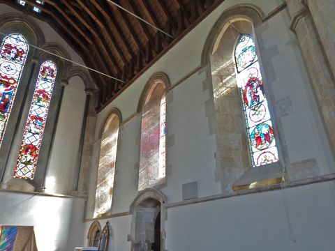 Architecture. Light pours through tall stained glass windows under the timbred ceiling of this church. The lowest level has an arched niche near the corner and doorway a little farther along the wall.