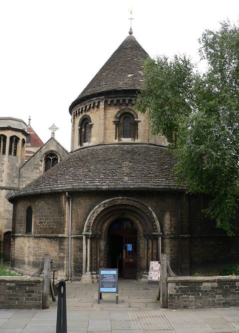 Architecture. A round stone church is accessed by an arched portal. At ground level, it is shaped like a wide lantern with a conical windowed roof above. 