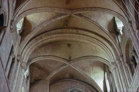 Architecture. Ribbed vaults spring from columns on an upper clerestory level of a church. Light comes in through arched windows tucked under the vaults.